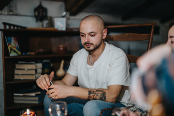 A serene man seated in a homey space exuding a relaxed and contemplative atmosphere with books, warm lighting, and artistic elements.