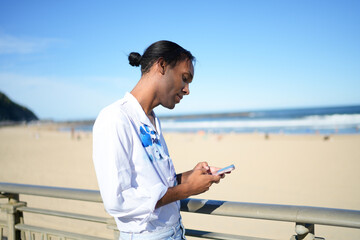 Gay man texting by beach, symbolizing pride and relaxation