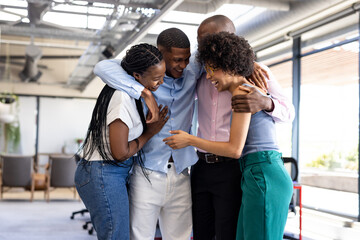 Diverse colleagues in office embracing and laughing, celebrating team success together