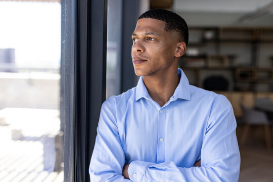 Businessman in blue shirt looking out window, contemplating future opportunities, copy space