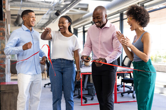 Diverse team celebrating office opening with ribbon cutting, smiling and clapping