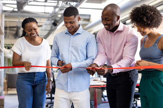 Diverse team celebrating office opening, cutting ribbon with smiles and excitement