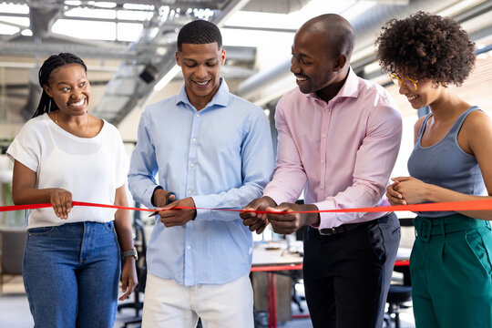 Cutting ribbon at office opening, diverse colleagues smiling and celebrating together