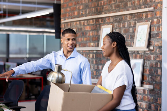 Diverse colleagues in office discussing while unpacking box, collaborating on project