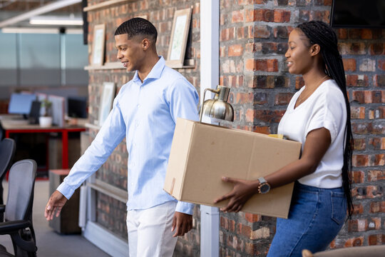 diverse colleagues carrying box and lamp while moving into new office