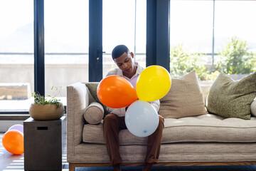 man sitting on sofa holding colorful balloons, looking thoughtful, at office
