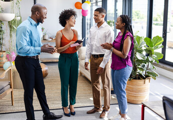 Diverse colleagues in office celebrating success, smiling and holding congratulatory card