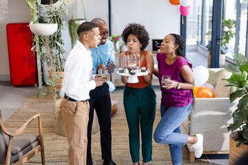 Diverse colleagues celebrating birthday in office, woman blowing candles on cake, smiling