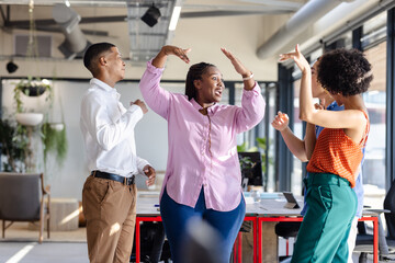 Diverse colleagues celebrating success with joyful dance in modern office space