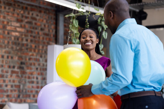 Celebrating with colorful balloons, diverse colleagues smiling in office