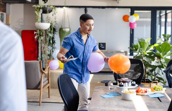 Man preparing office farewell party with balloons and cake on table