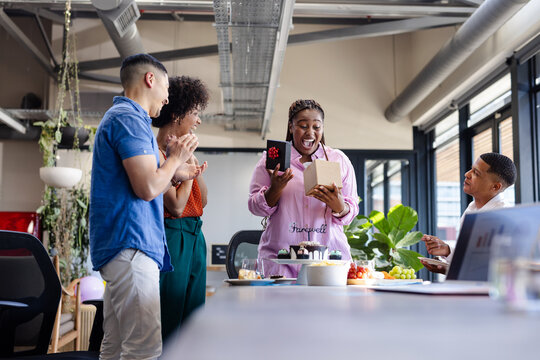 Diverse colleagues celebrating with gifts and cake in modern office farewell party