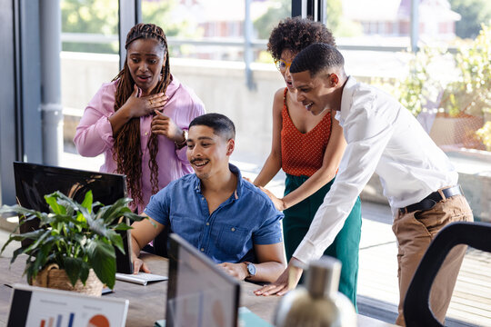 Diverse team collaborating around computer, discussing project in modern office