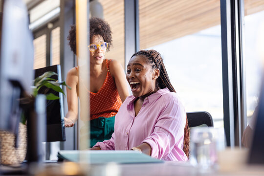 Excited woman at office desk discussing project with colleague