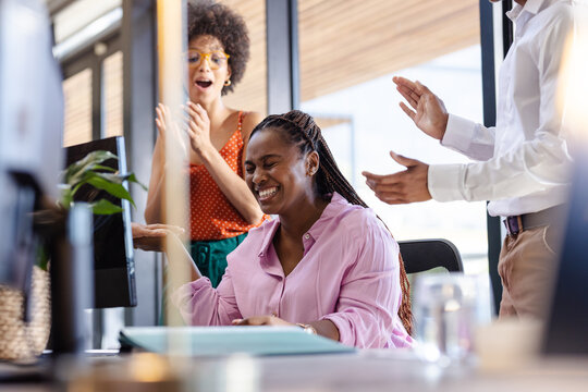 Celebrating success, woman in office with diverse colleagues clapping joyfully