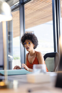 Surprised woman in office looking at laptop, wearing glasses and polka dot top, copy space