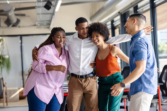 Celebrating teamwork success, diverse colleagues embracing and laughing in modern office