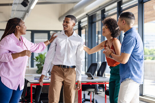 Diverse colleagues in office celebrating success, smiling and congratulating each other