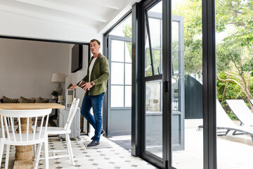 Man holding tablet walking through modern home with open patio doors