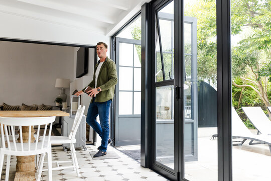 Man holding tablet walking through modern home with open patio doors