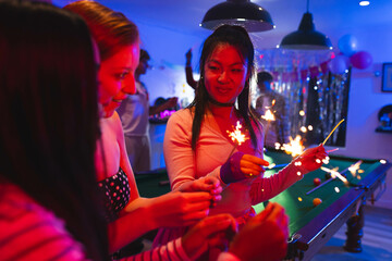 Diverse Teenage friends celebrating with sparklers at lively party near pool table, at home