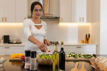 Woman preparing fresh salad in modern kitchen, smiling and enjoying cooking, copy space, at home