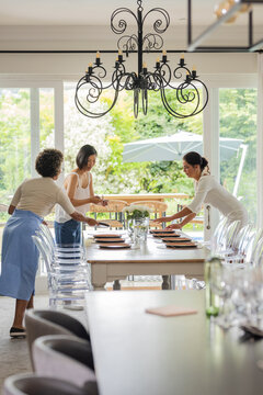 Arranging plates and decor, women setting elegant table for small casual wedding celebration, at hom