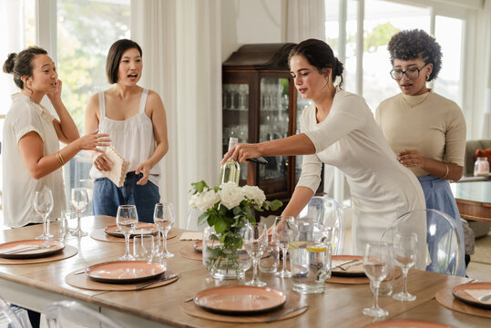 Arranging flowers and glasses, women preparing elegant dining table for small casual wedding, at hom