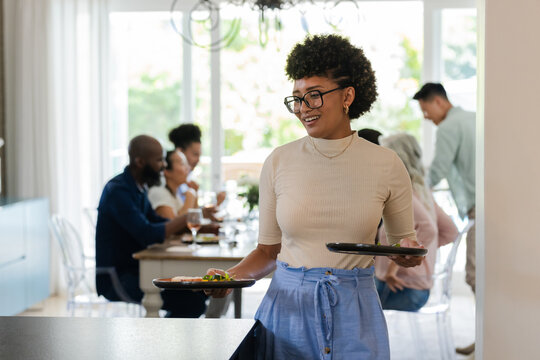 Smiling woman serving food to guests at lively small casual wedding reception indoors, at home