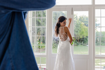 Bride in elegant lace gown posing joyfully by sunlit window on wedding day
