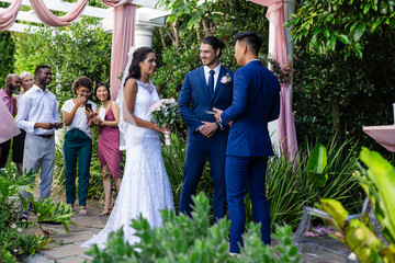 Bride and groom exchanging vows outdoors, surrounded by joyful friends and family