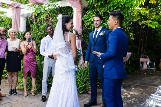 Bride and groom exchanging vows outdoors, surrounded by joyful friends and family