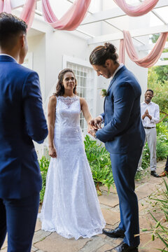 Bride and groom exchanging rings outdoors, surrounded by joyful friends