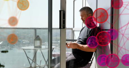 Globe of digital icons against caucasian senior man using smartphone in the balcony at home
