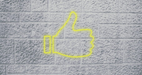 Neon yellow thumbs up sign glowing on textured brick wall background