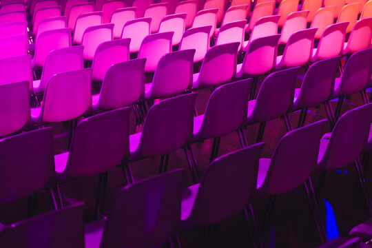 Rows of empty chairs in pink and purple lighting at a conference of AI