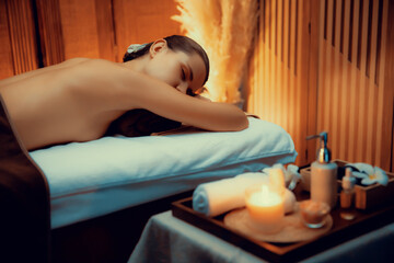 Aromatherapy massage ambiance or spa salon composition setup with focus decor candles and spa accessories on blurred woman enjoying blissful aroma spa massage in resort or hotel background. Quiescent