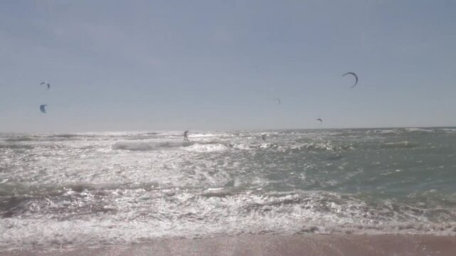 Kitesurfers glide over the waves enjoying on a windy day at the Canos de Meca, a wild, scenic beach along Vejer de la Frontera's coast in Cadiz, Andalusia, Spain.