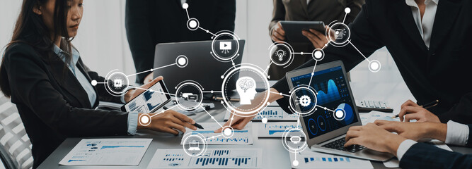 A diverse business team collaborates in a modern office, discussing AI technology solutions and analyzing data visualizations on multiple devices, driving innovation and strategy. Amity