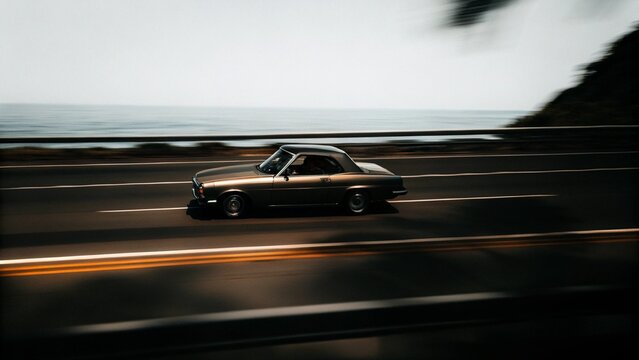 Fototapeta Vintage car going in a high way next to the ocean