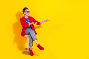 Stylish mature woman in vibrant outfit gesturing enthusiastically against a vivid yellow backdrop,...