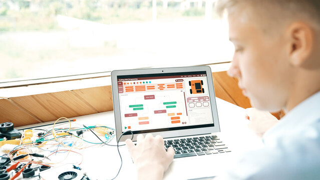 Caucasian student looking at laptop screen while coding engineering prompt or programing system. Back view of smart teenager working by using computer and electronic tool at STEM class. Edification.