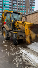 Yellow backhoe loader parked on snowy urban street, construction machinery, winter infrastructure maintenance equipment