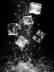 Dramatic monochrome capture of ice cubes in dynamic splash against stark black backdrop for refreshing beverage concept