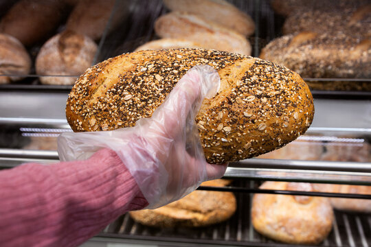 Hand Selecting Fresh Multigrain Bread in Bakery Display
