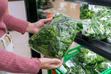 Shopper holding packaged fresh spinach at grocery store