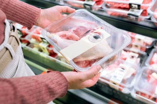 Customer choosing packaged chicken in supermarket aisle