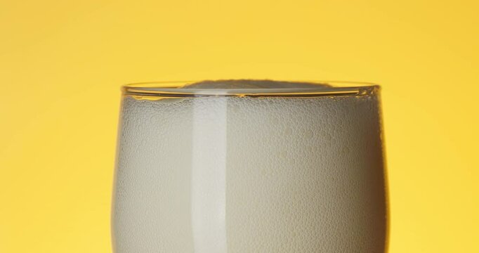 Beer is poured into a glass beaker from a bottle on a yellow background