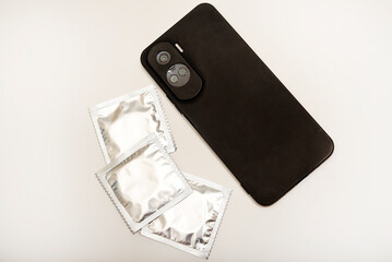 Condoms in shiny packaging and a black smartphone.