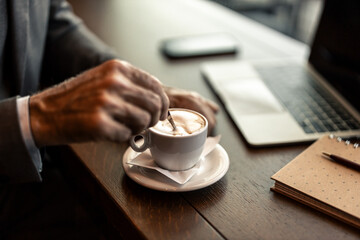 Businessman Stirring Coffee While Working on Laptop at Cafe